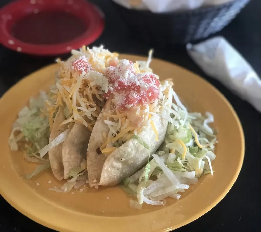 Two hard-shell tacos with lettuce, cheese, and salsa on a yellow plate.