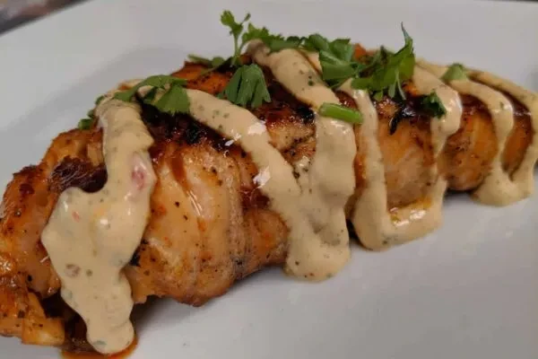 Golden-brown grilled protein with creamy herb sauce and fresh garnish.