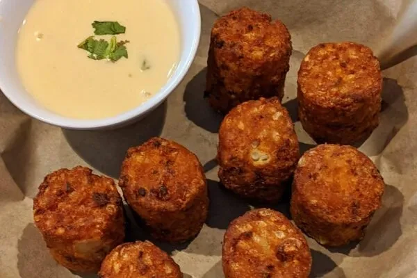 Golden-brown crispy fried bites with yellow dipping sauce and herbs.