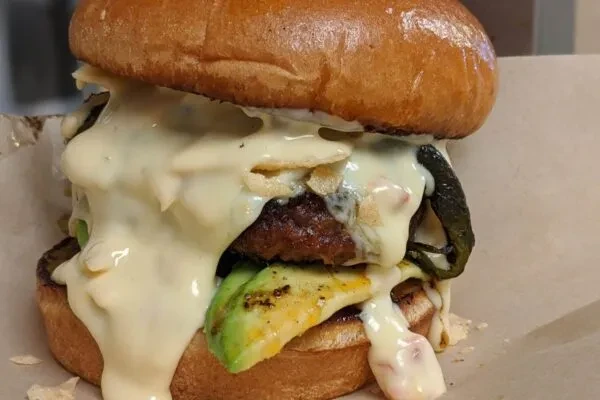Gourmet burger with melted white cheese, avocado, and roasted poblano.