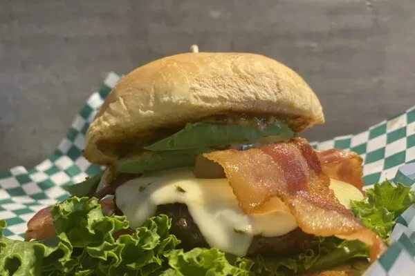 Burger with bun, patty, melted cheese, bacon, avocado, and lettuce.