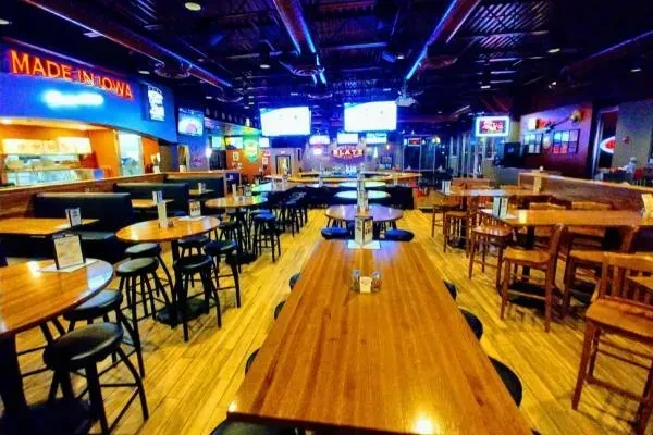 Empty, spacious modern sports bar with blue-purple lighting and TVs.