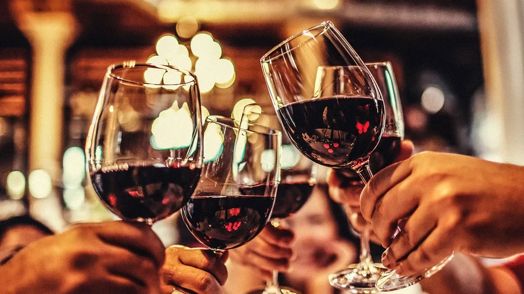 Hands holding red wine glasses raised in a celebratory toast.