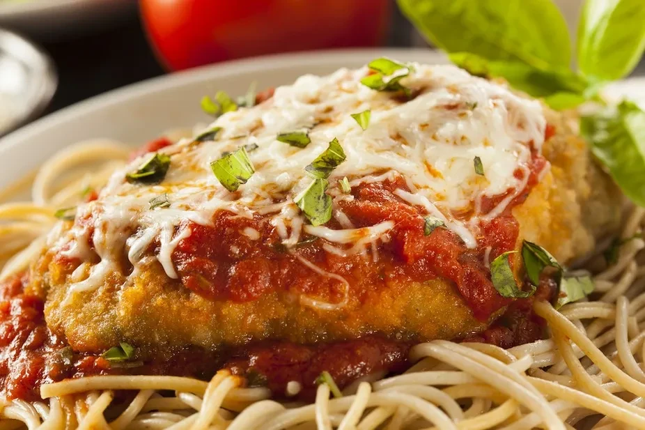Close-up: Breaded parmesan cutlet with marinara, cheese, and basil on spaghetti.