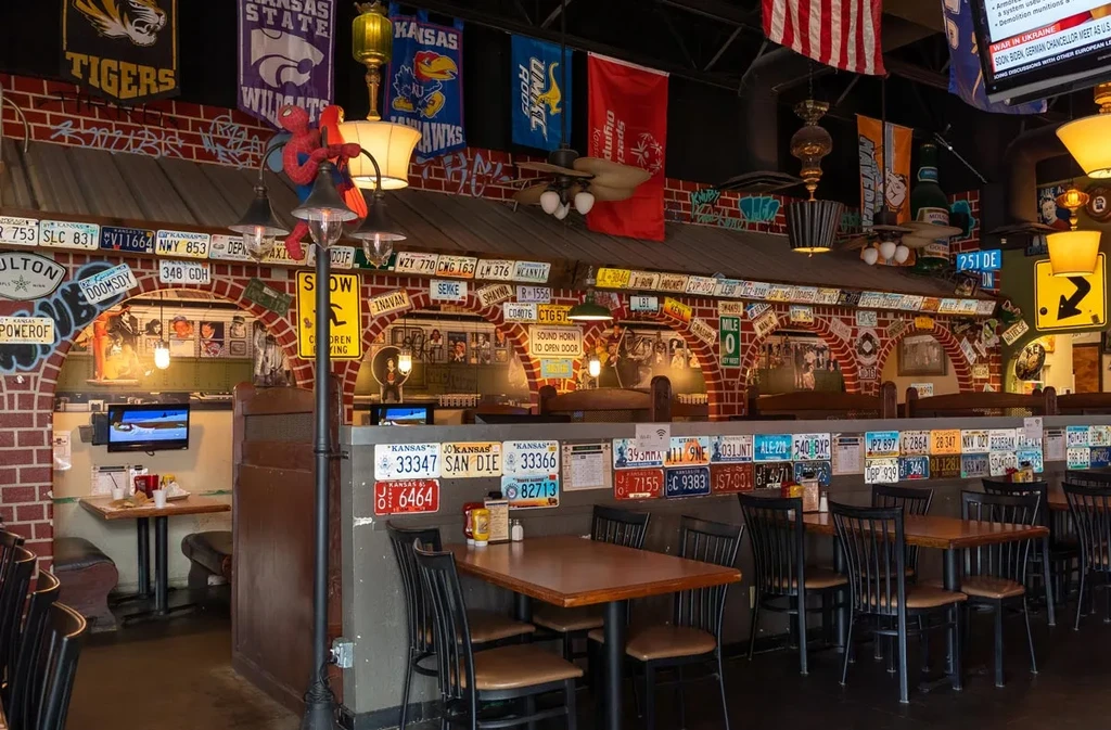 Restaurant interior with brick wall, colorful license plates, and sports banners.