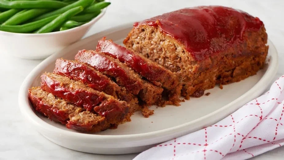 Sliced glazed meatloaf with green beans on a white platter.