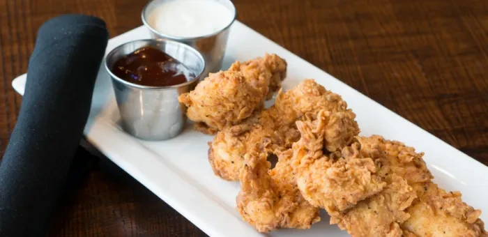 Plate of golden-brown fried chicken tenders with two dipping sauces.