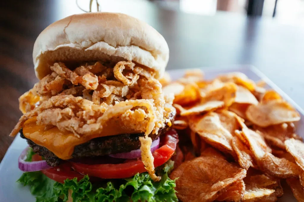Close-up of gourmet burger with cheese, fried onions, and potato chips.