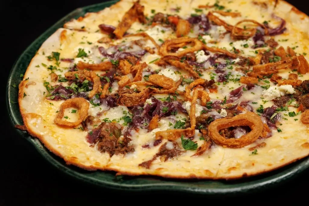 Thin-crust pizza with cheese, meat, red onion, crispy shallots, and herbs.