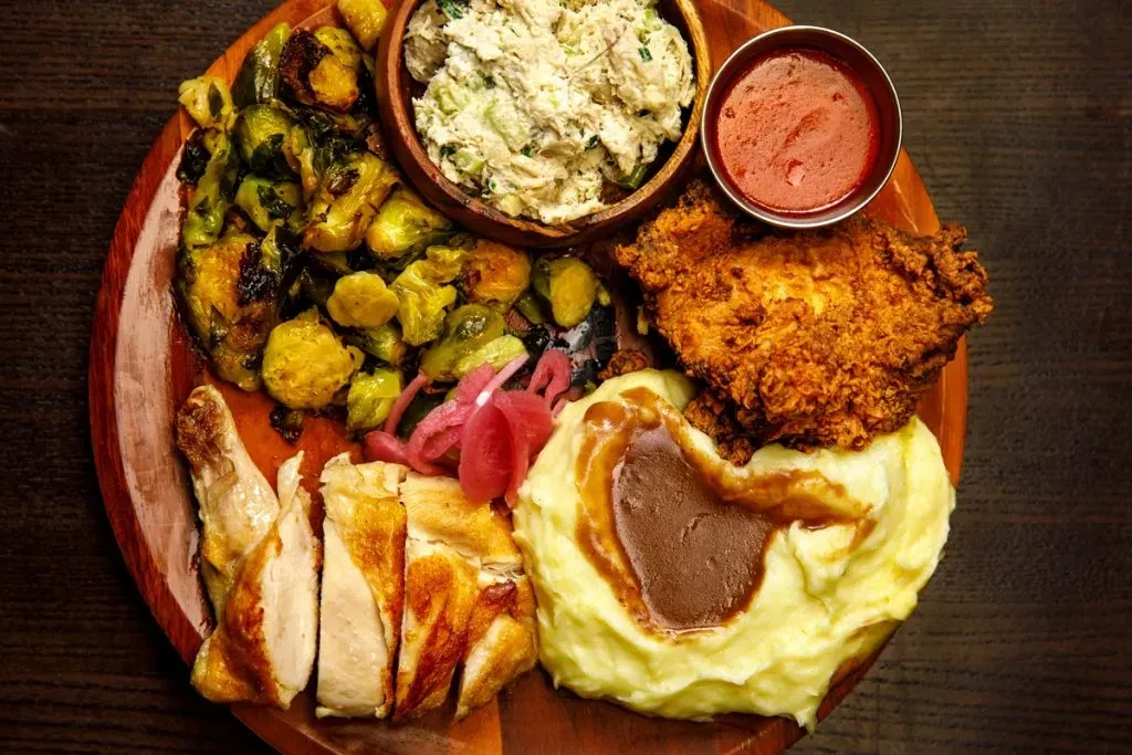 Rustic platter of fried chicken, mashed potatoes, brussels sprouts, creamy salad.