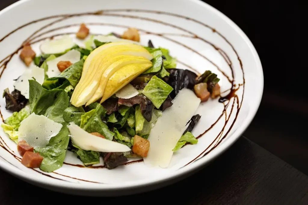 Vibrant mixed green salad with pear, cheese, bacon, and balsamic.