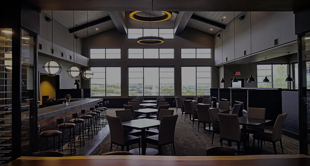 Empty, spacious, modern restaurant with bar, tables, and large windows.