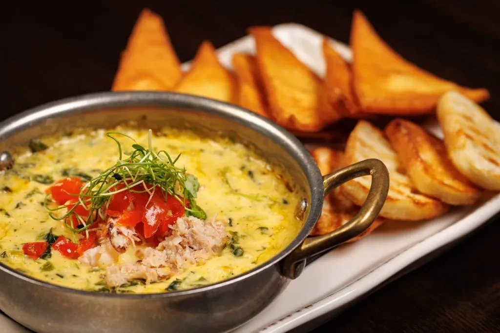 Seafood dip in rustic pot garnished with microgreens, bread, and chips.