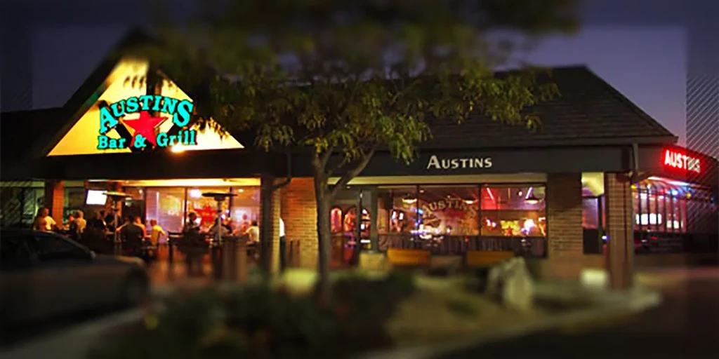 Illuminated Austin's Bar & Grill exterior at night, with patrons on patio.