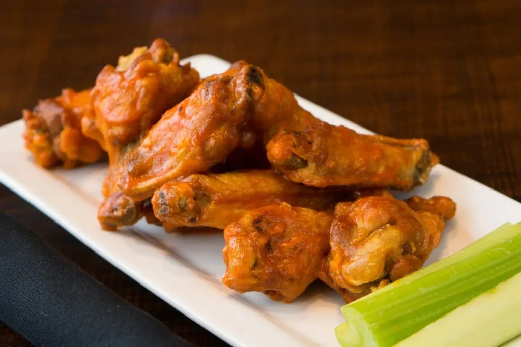Plate of glossy orange-red Buffalo wings and crisp green celery.