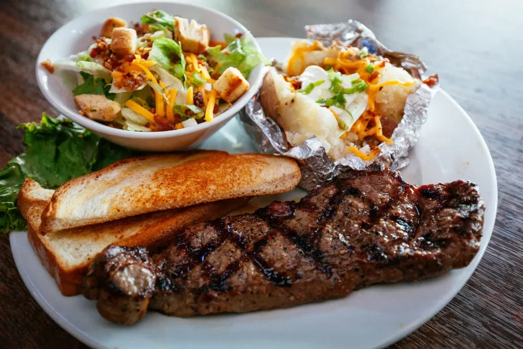 Grilled steak, toasted bread, side salad, and loaded baked potato.