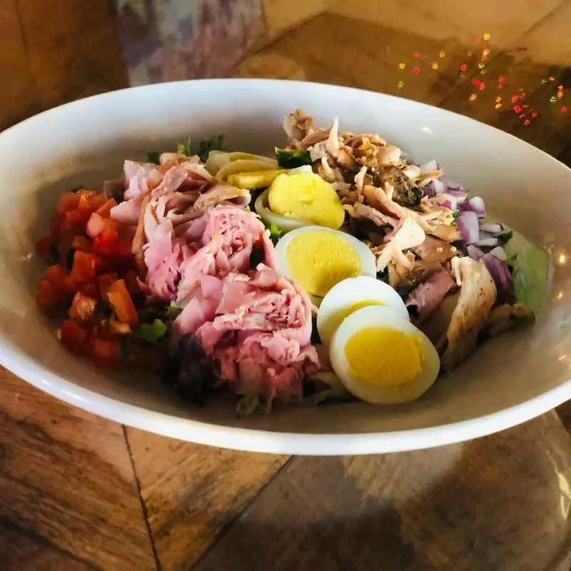Colorful Cobb salad with chicken, ham, eggs, and tomatoes in a bowl.