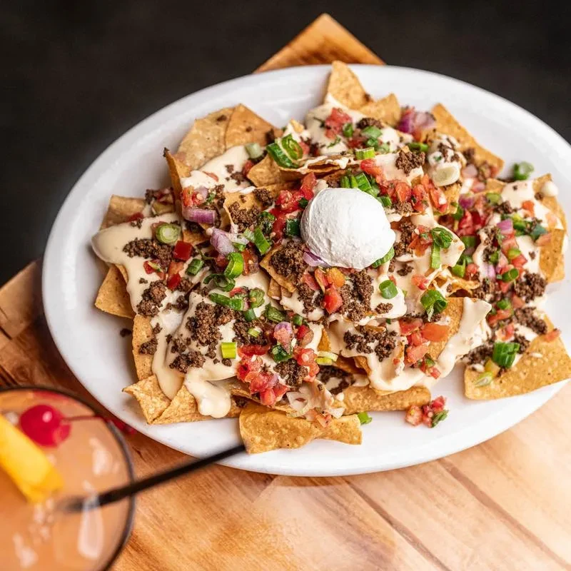 Large plate of nachos with meat, cheese, vegetables, and sour cream.