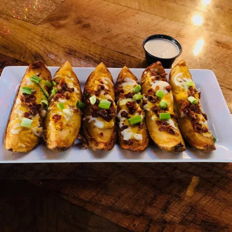 Six loaded potato skins with cheese, bacon, green onions, and white sauce.