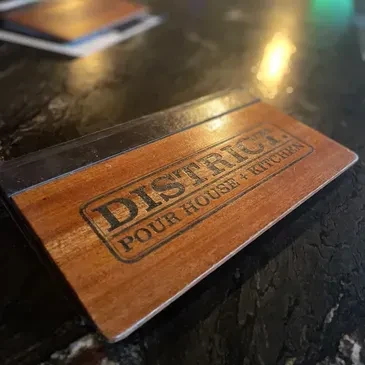 Dark wooden check presenter with 'DISTRICT POUR HOUSE + KITCHEN' logo.