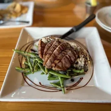 Sliced seared meat, risotto, green beans, dark sauce on white plate.