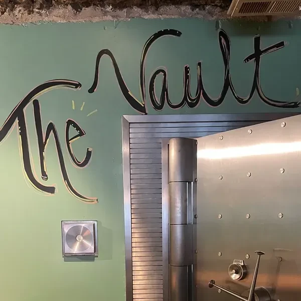 Partially open metallic vault door and "The Vault" sign in a restaurant.