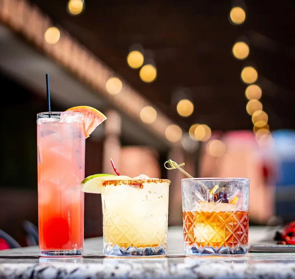 Three diverse cocktails, each in a unique glass, on a reflective counter.