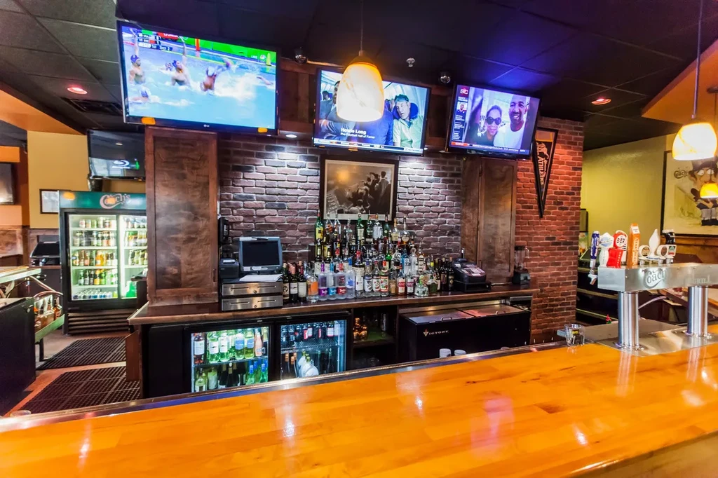A well-stocked bar with brick wall, three TVs, and many liquor bottles.