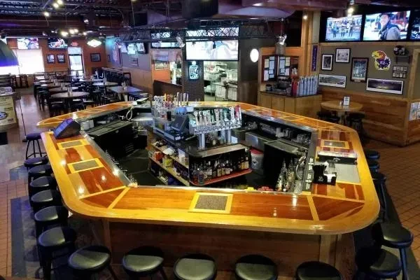 Casual sports bar interior with a large wooden bar and multiple TVs.