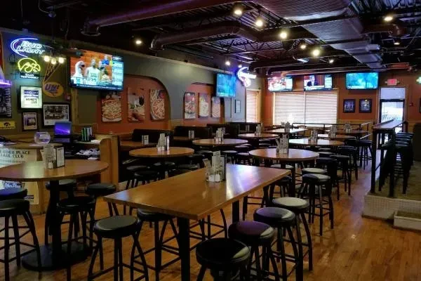 Dimly lit sports bar interior with wooden tables, booths, and TVs.