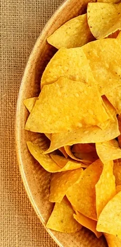 Golden tortilla chips piled high in a rustic bowl on burlap.
