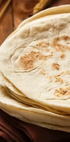 Close-up of a stack of golden-spotted flatbreads on a rustic board.