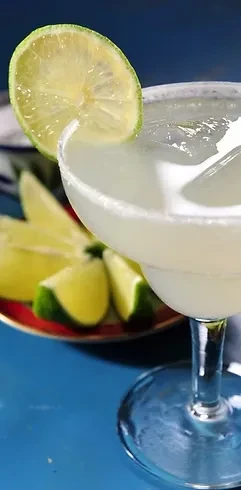 Margarita in glass with salted rim, lime wheel, on blue surface.