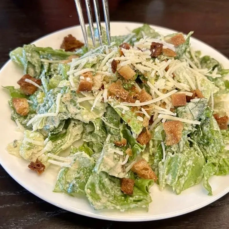 Overhead close-up of Caesar salad with lettuce, croutons, Parmesan, and fork.