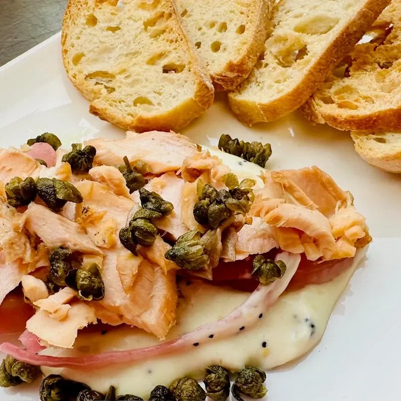 Flaked salmon with capers, creamy sauce, pickled onion, and toasted bread.