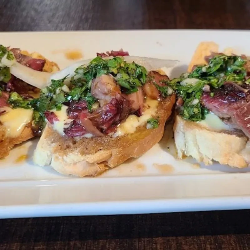 Three bruschetta with medium-rare meat, melted cheese, and green herbs.