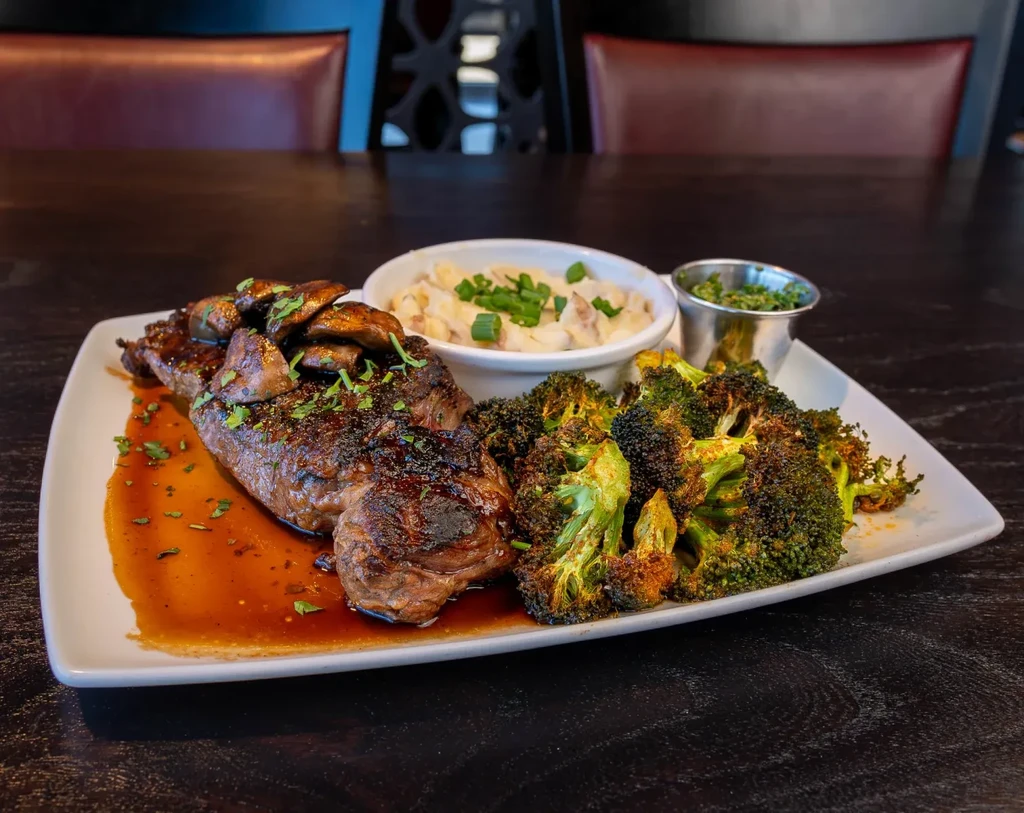 Grilled steak, mushrooms, broccoli, mashed potatoes, and green herb sauce plated.