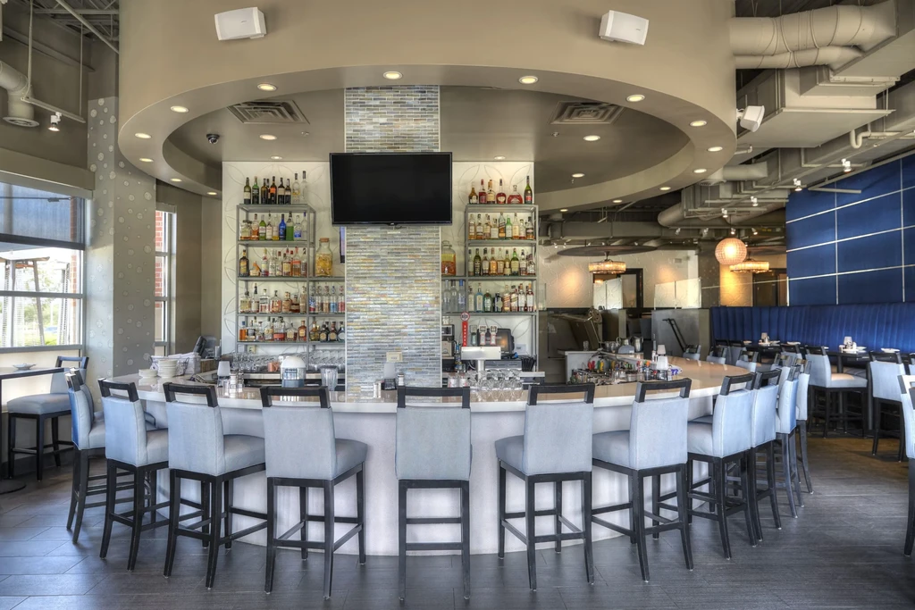 Modern restaurant interior: semi-circular bar, liquor bottles, and adjacent dining area.