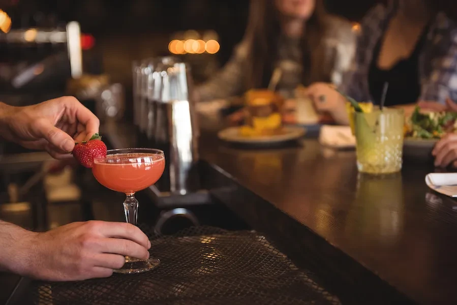 Bartender garnishes a pink cocktail with a fresh strawberry.