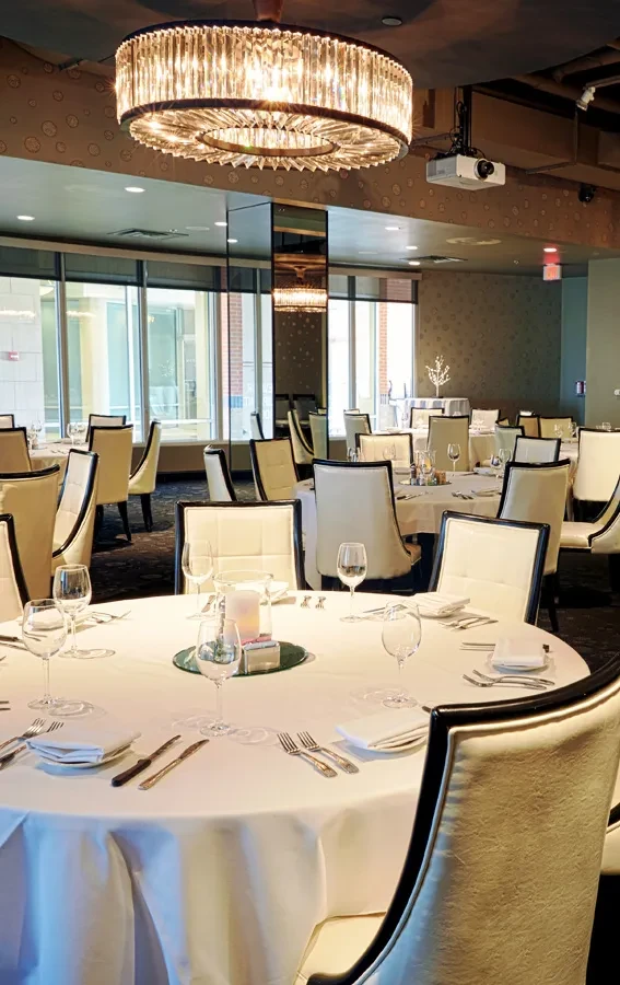 Elegant restaurant dining room with meticulously set tables and a chandelier.