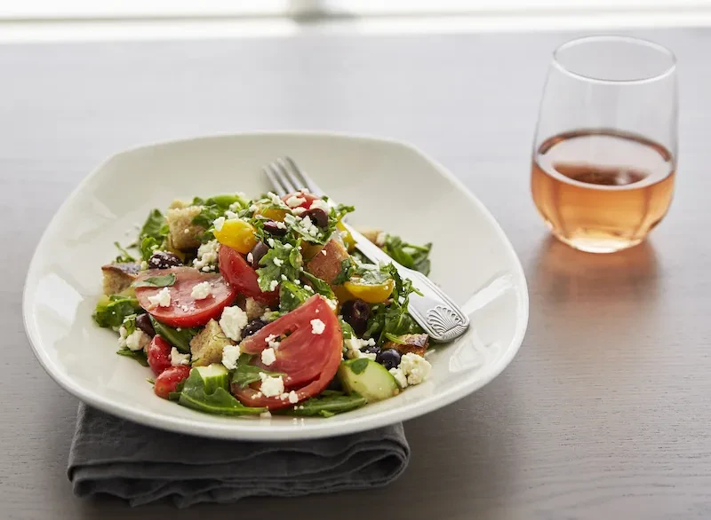 Vibrant Greek salad with tomatoes, feta, olives, and rosé wine.
