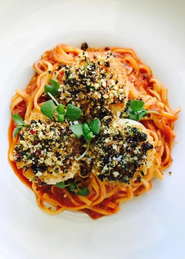 Linguine with pan-seared crusted scallops, tomato sauce, and microgreens.