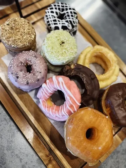 Ten colorful gourmet donuts with diverse toppings on a wooden tray.