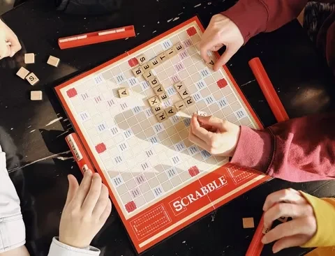Overhead view of a Scrabble game in progress, with tiles and hands.