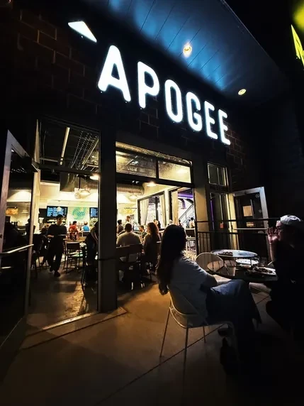 APOGEE restaurant exterior at night; brightly lit sign, warm interior.