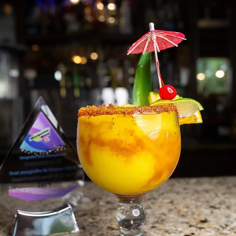 Garnished chili-mango margarita next to "Best Margarita in Houston" award.
