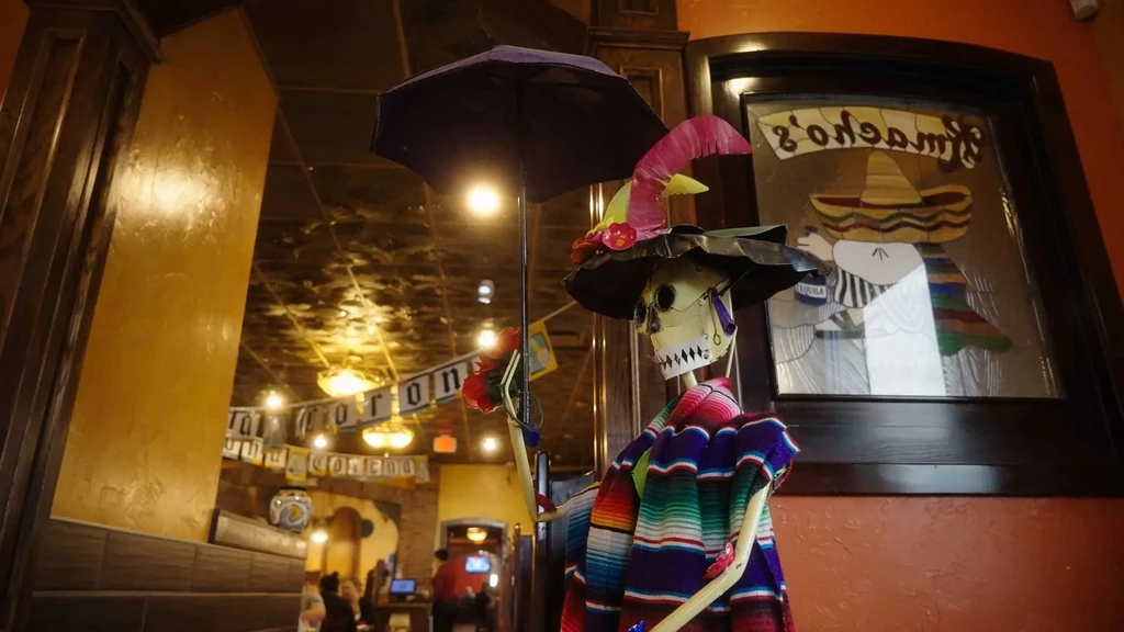 Colorful skeleton in serape, hat, holding umbrella, in a Mexican restaurant.
