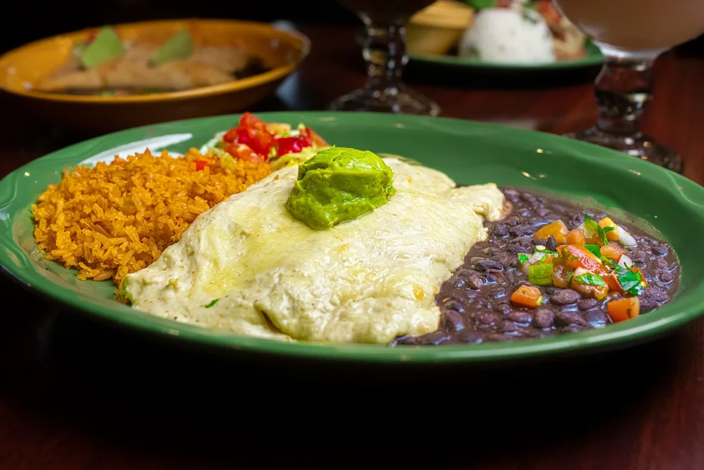 Green enchiladas, orange rice, and black beans with colorful salsa.