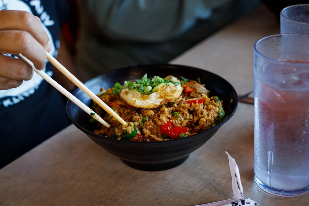 Hands using chopsticks to eat fried rice with a sunny-side-up egg.