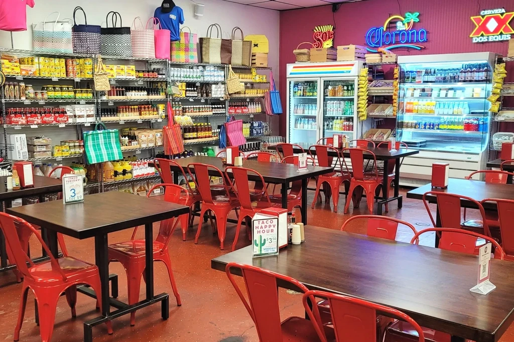 Restaurant interior with red tables, retail shelves, and Latin-themed neon signs.